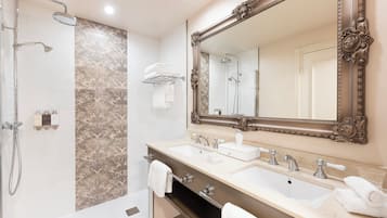 A bathroom with a shower, two sinks, a large mirror, and a towel rack.