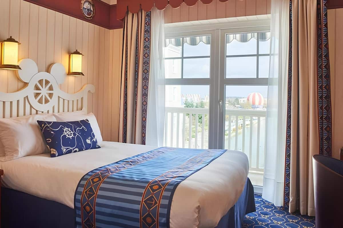A bed with a nautical-themed headboard, two wall-mounted lamps, and a view of a balcony with a hot air balloon.