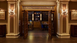 A warmly lit library with a sign reading "Compass Club" and a wooden desk with a chair. - Disney Newport Bay Club (Coupvray)