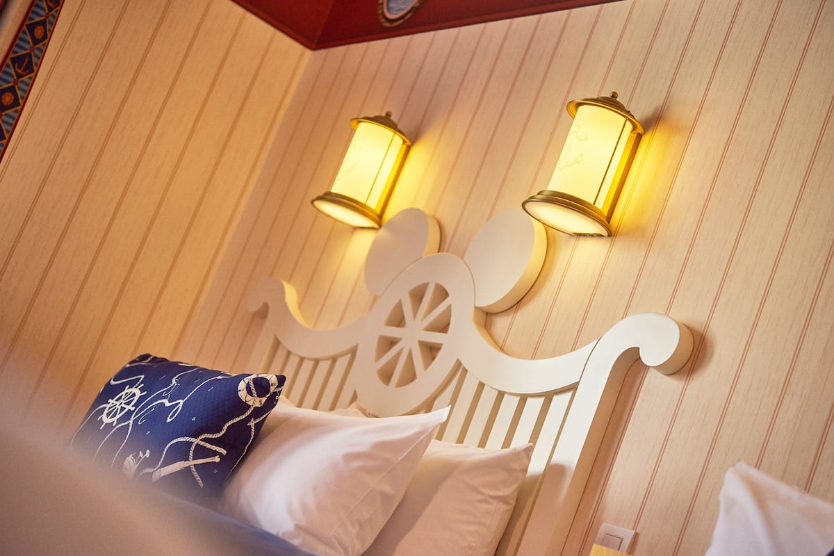 A hotel room with a wooden headboard, two wall-mounted lamps, and a decorative pillow.