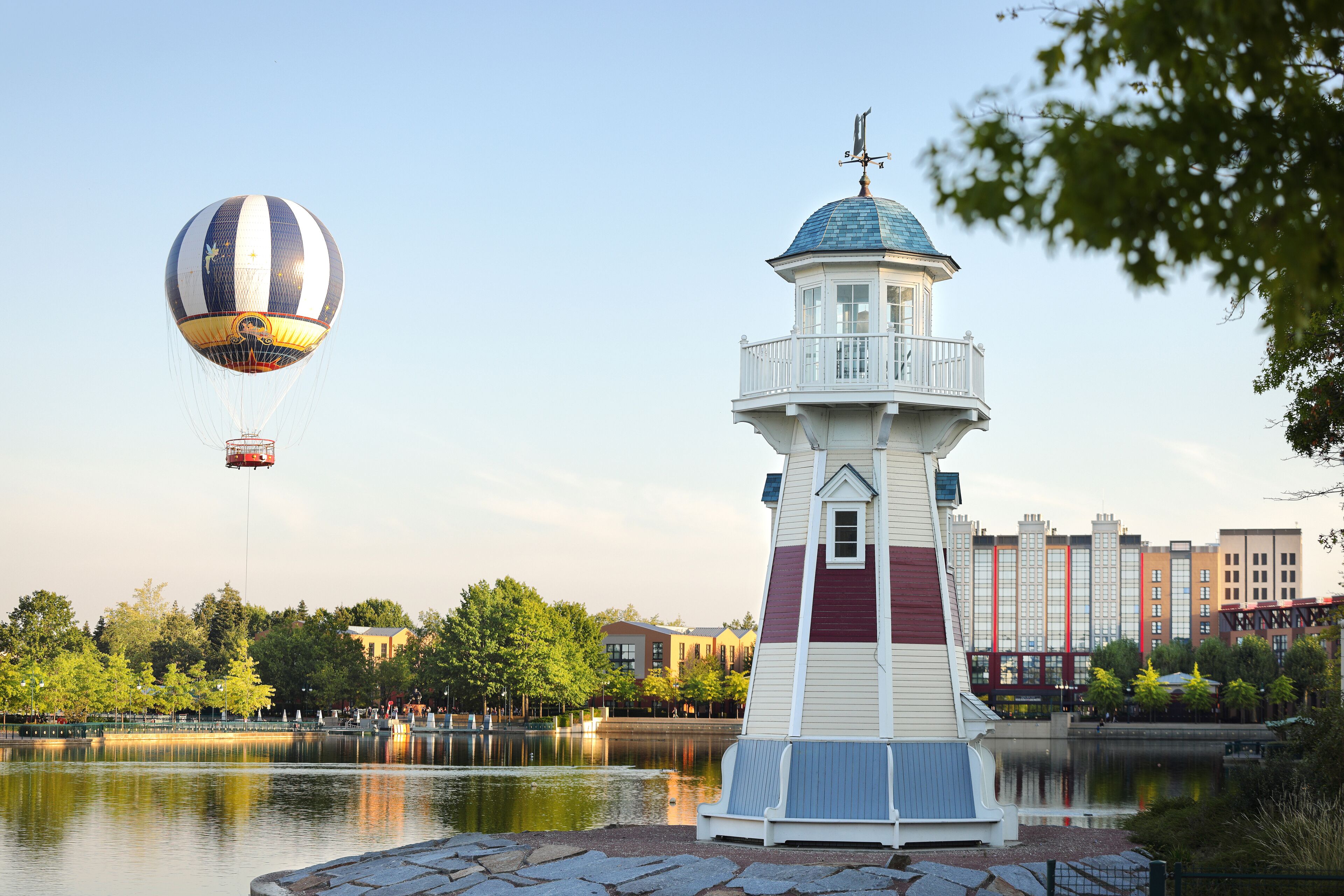 Een vuurtoren aan een rustig meer met een luchtballon op de achtergrond.