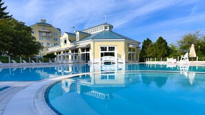 Une grande piscine avec un pont, entourée d’une clôture blanche et de chaises longues.