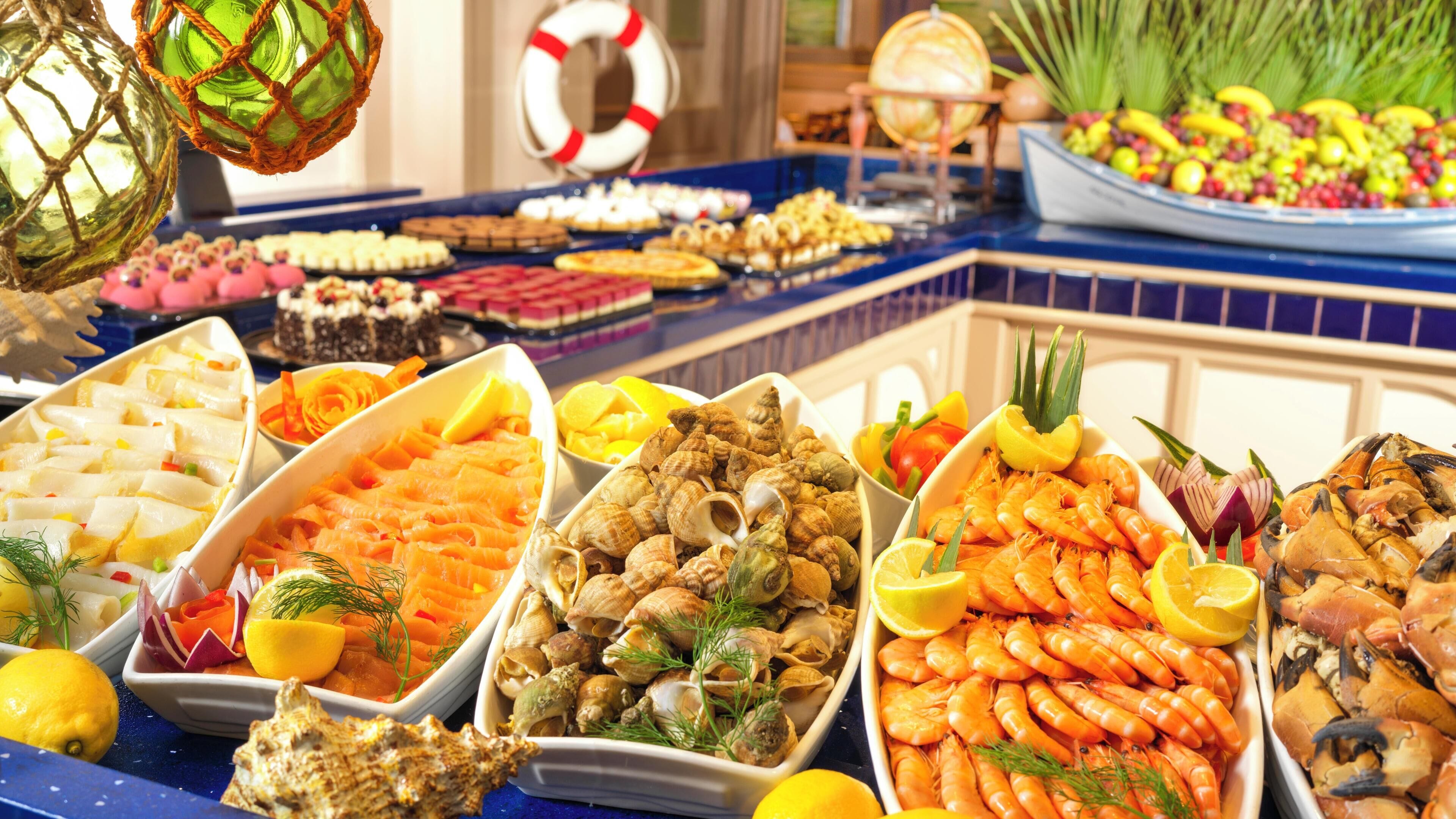 Un bufé con diversos platos de mariscos, incluyendo camarones, vieiras y ostras, dispuestos sobre una barra de azulejos azules.