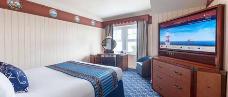 A hotel room with a bed, a desk, a dresser, and a television displaying a lighthouse scene.