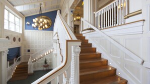 Un magnifique escalier avec des rampes blanches et des marches en bois, menant à un palier agrémenté d’un lustre.