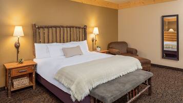 A hotel room with a large bed, two bedside tables with lamps, a chair, a bench, and a mirror on the wall.