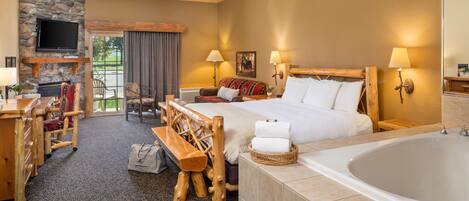 A hotel room with a large bed, a wooden bench, a fireplace, a television, and a bathtub.