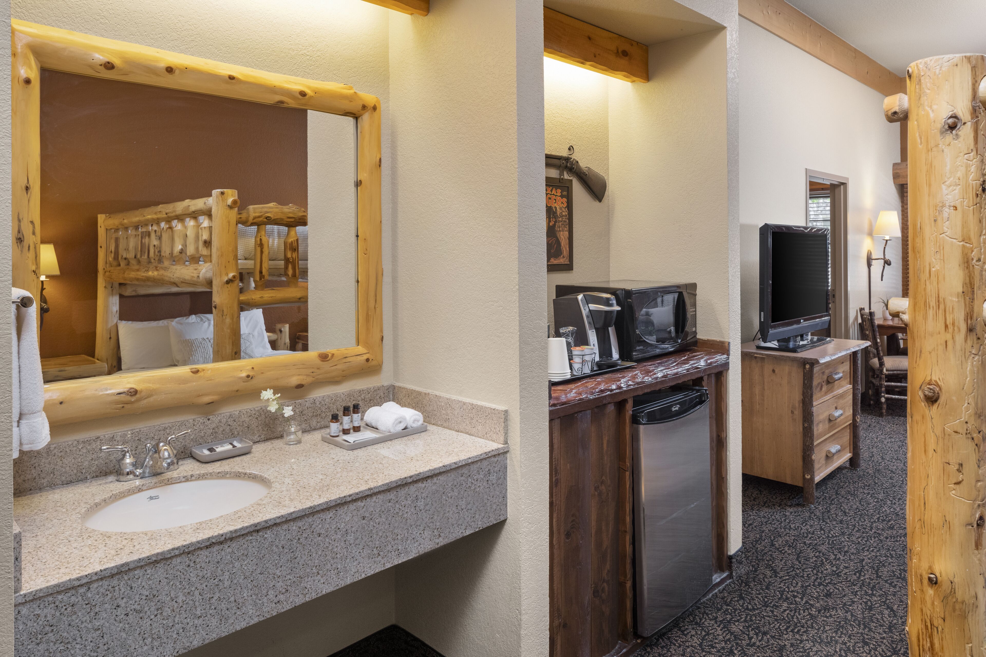 A bathroom with a wooden-framed mirror, a sink with toiletries, and a shower area.