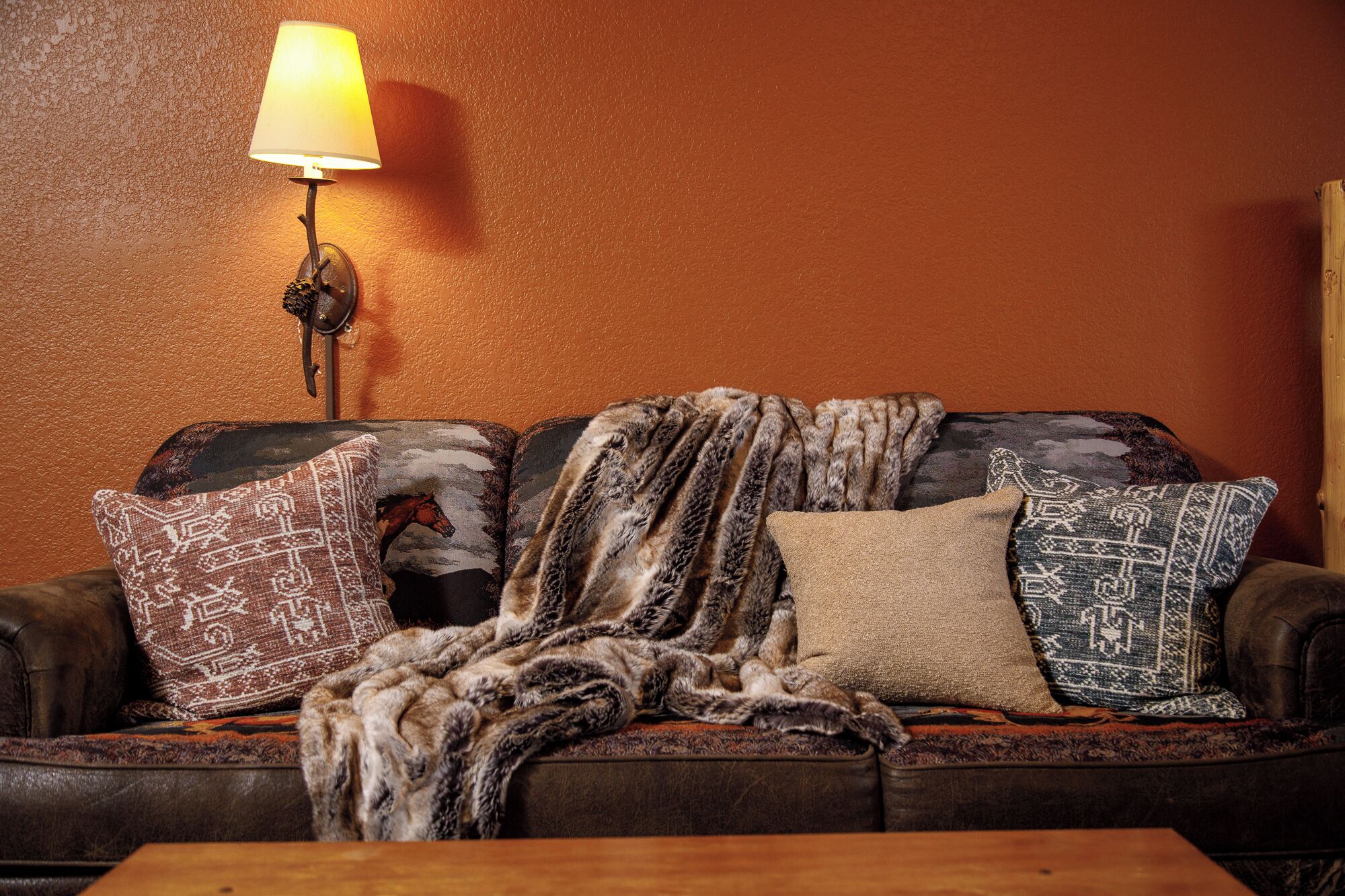 A cozy living room with a brown leather sofa, patterned throw pillows, and a fur throw.