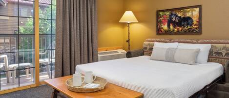 A hotel room with a large bed, a table with a tray of items, a lamp, and a painting on the wall.