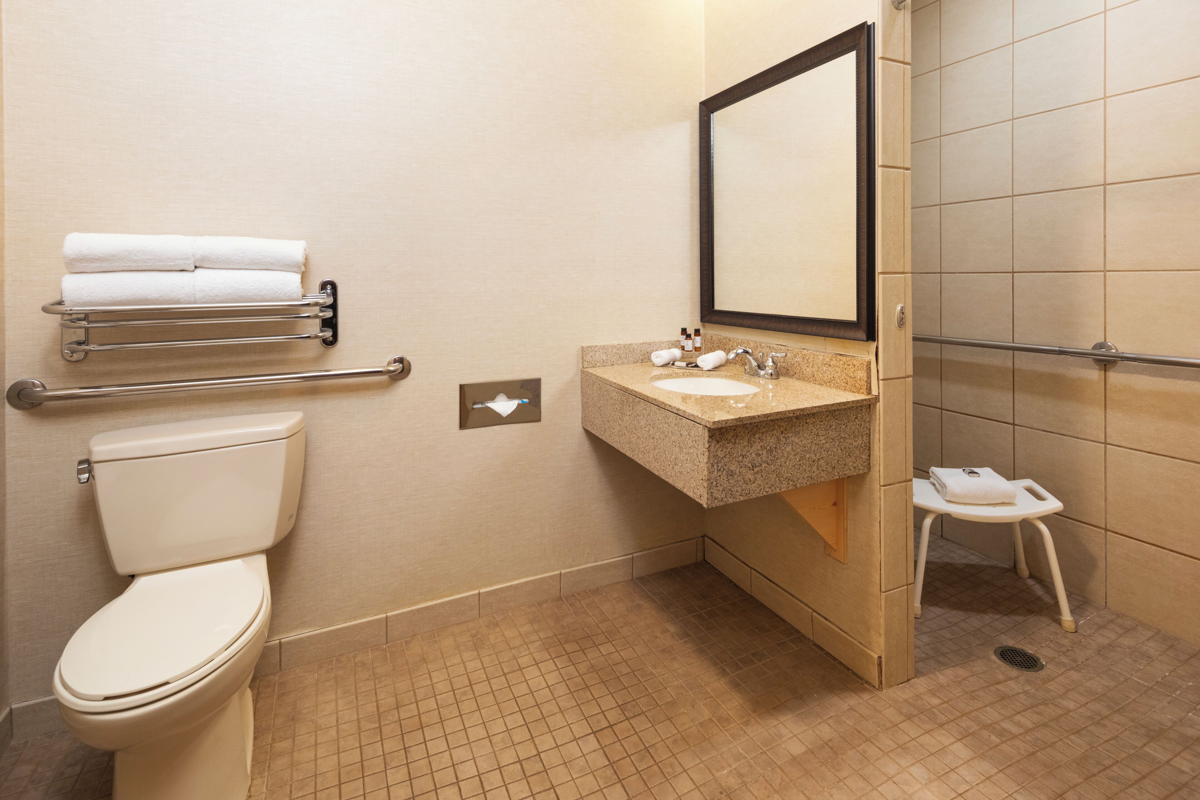A bathroom with a toilet, sink, towel rack, and a small stool.