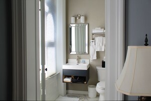 A bathroom with a white sink, mirror, and toilet. There is a towel rack above the sink and a trash can next to the toilet.