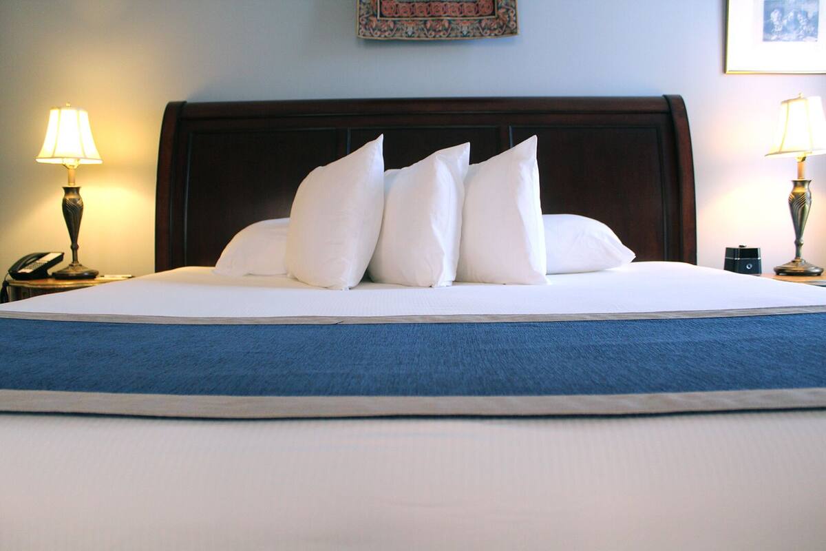 A neatly made bed with white linens and pillows, a dark wooden headboard, and two bedside lamps on either side.