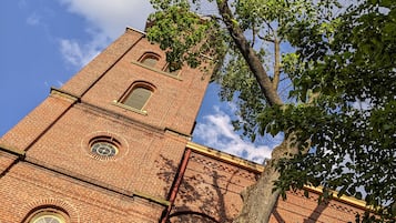 A brick tower with a clock and arched windows, surrounded by trees.