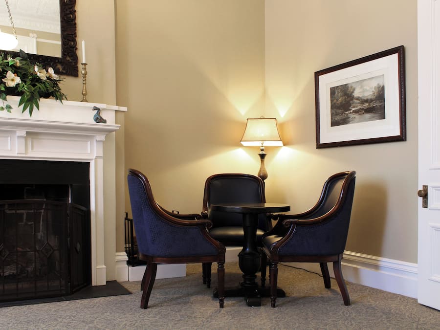 A room with a fireplace, a table with two chairs, a lamp, and a framed picture on the wall.