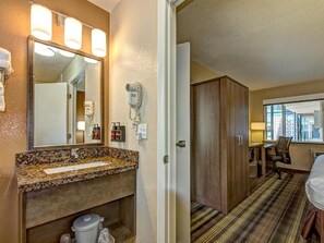 A hotel bathroom with a granite countertop sink, a mirror with lights, a hairdryer, and a toilet.