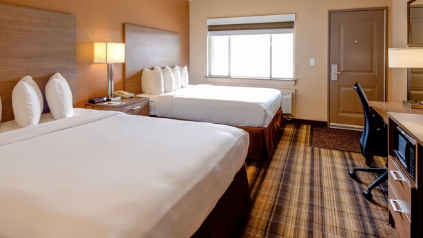 A hotel room with two beds, a desk, a chair, a lamp, and a window. - Boulder University Inn (Boulder)