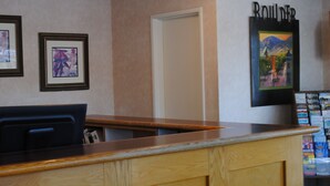A reception area with a wooden counter, framed artwork on the wall, and a door. - Boulder University Inn (Boulder)