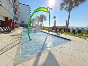 A swimming pool with a water fountain, lounge chairs, and a view of the sea.