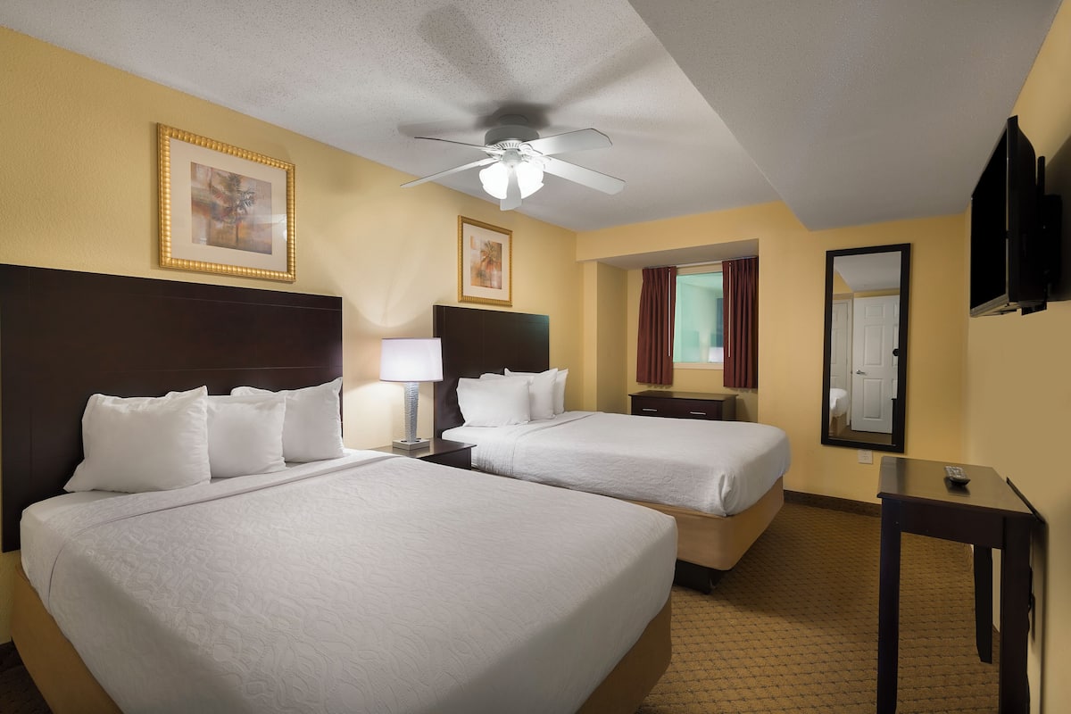 A hotel room with two beds, a ceiling fan, a TV, and a mirror.