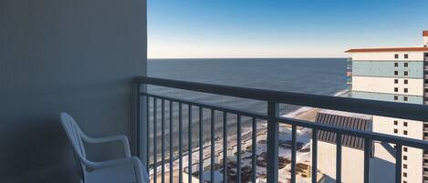 En balkon med hvide plaststole, gelænder og udsigt over havet og bygninger.