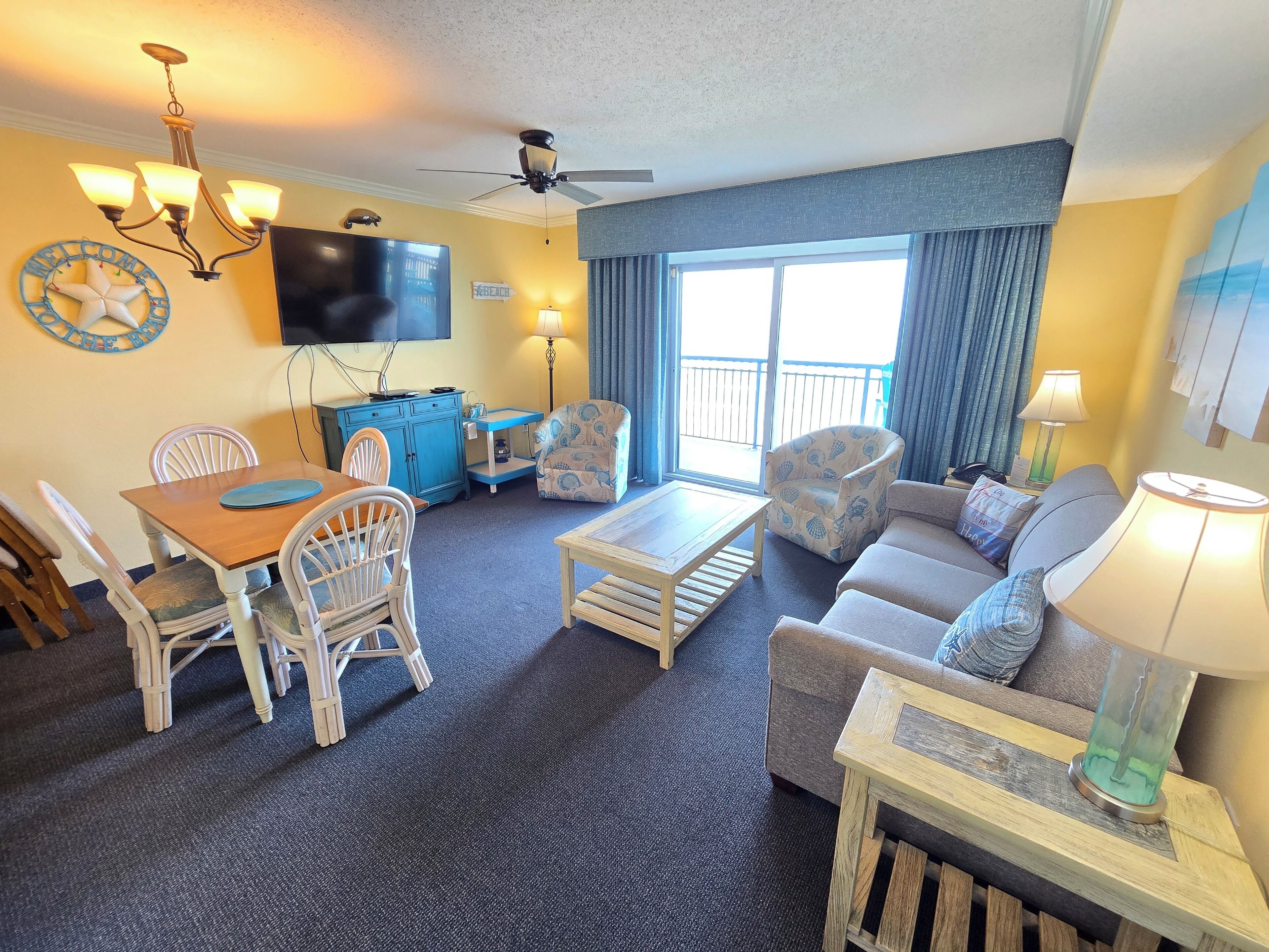 Habitación de hotel con comedor, sofá, televisor y balcón con cortinas.