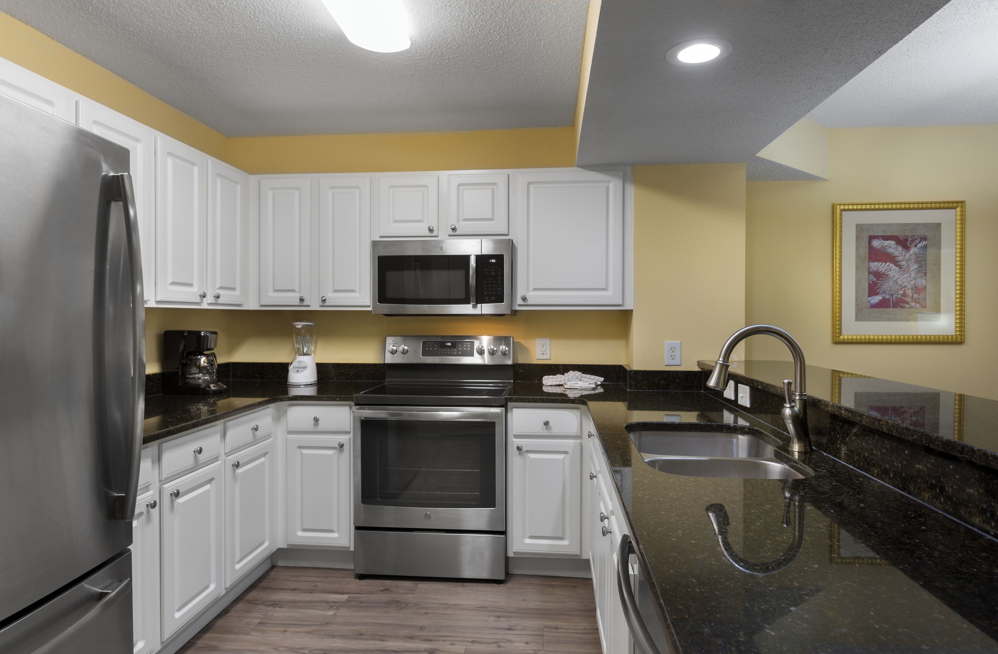 A modern kitchen with white cabinets, stainless steel appliances, a granite countertop, and a yellow accent wall.