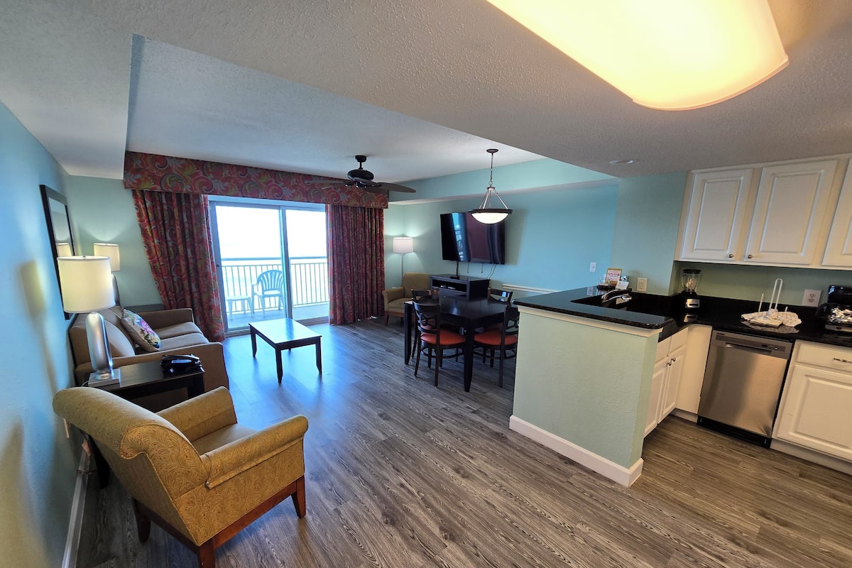 A hotel room with a living area, dining area, and kitchenette.