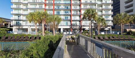 A multi-story hotel with balconies, a wooden walkway, and palm trees.