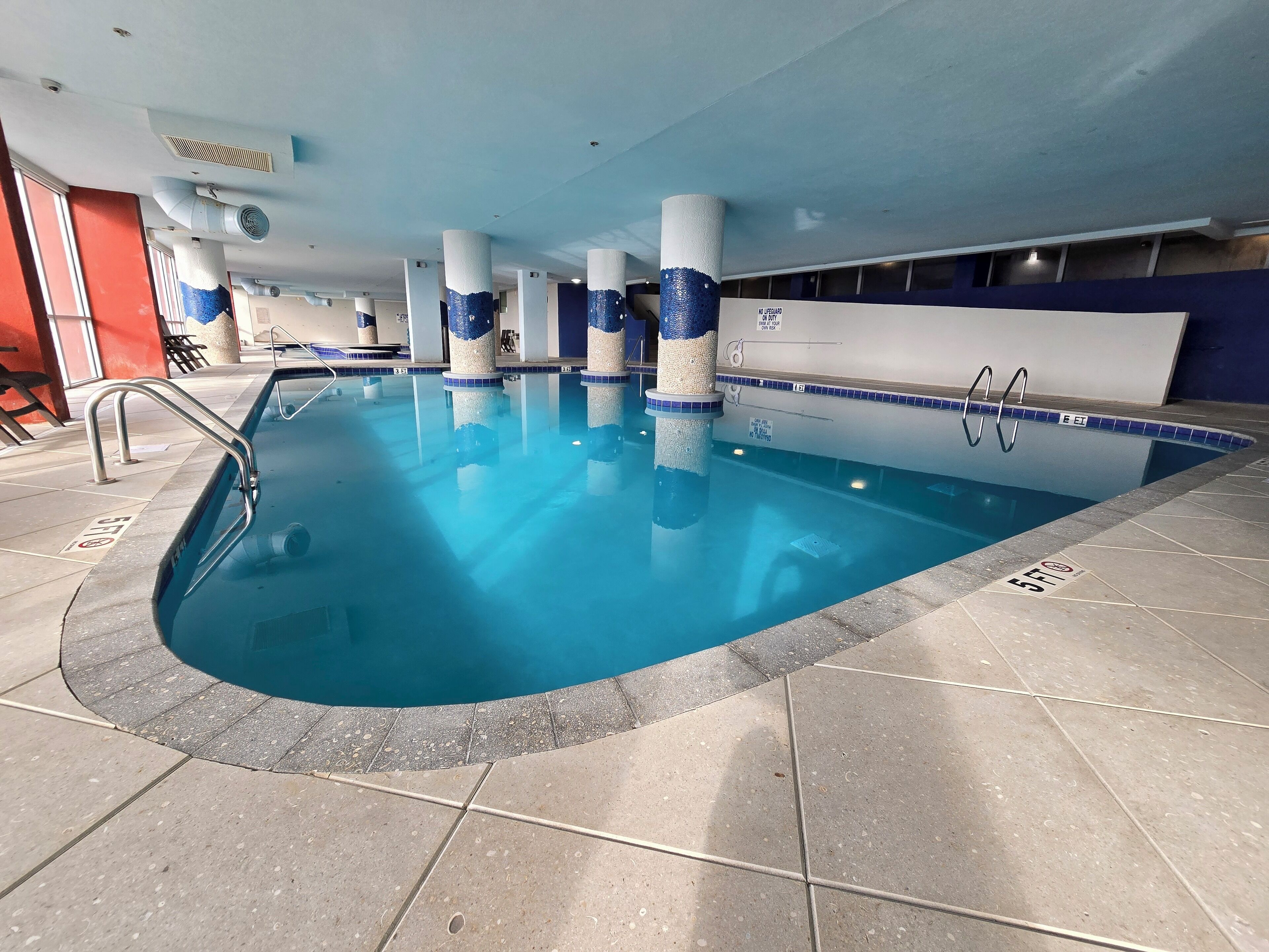 Ein Hallenbad mit klarem Wasser, gefliestem Boden und Sicherheitshinweisen.