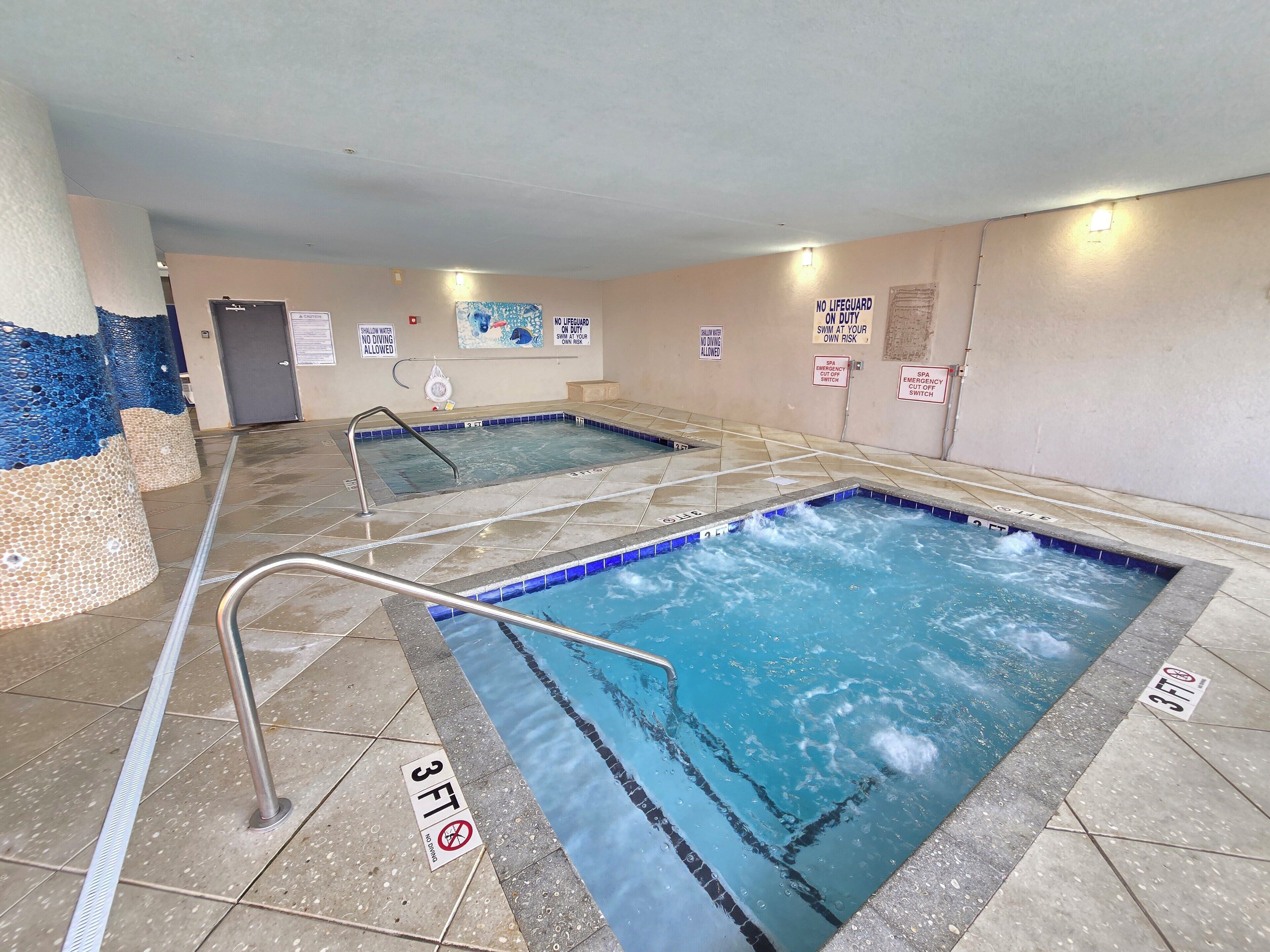 An indoor swimming pool with clear water, tiled floors, and safety signs.