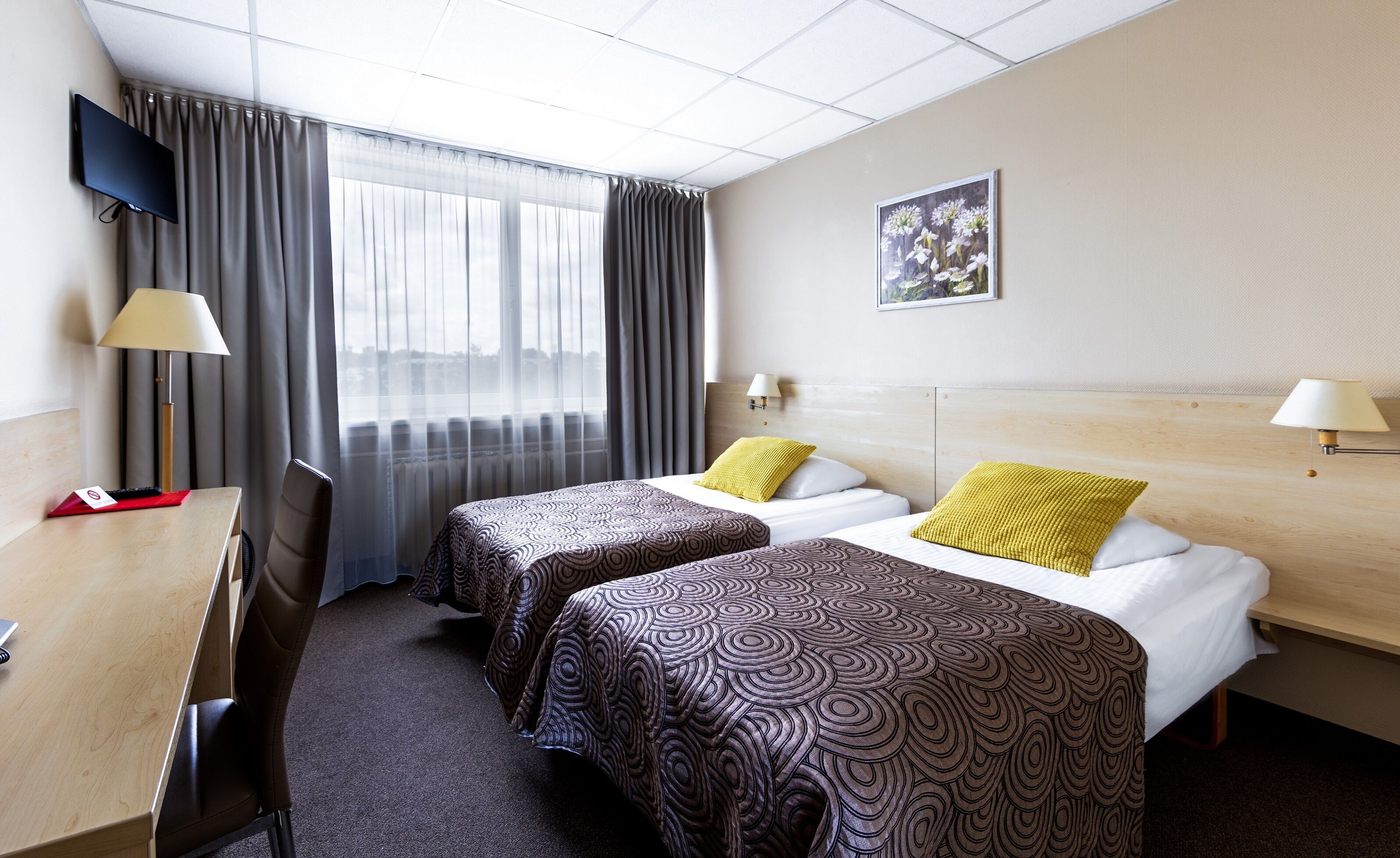 A hotel room with two beds, a desk, a TV, and a window with curtains.