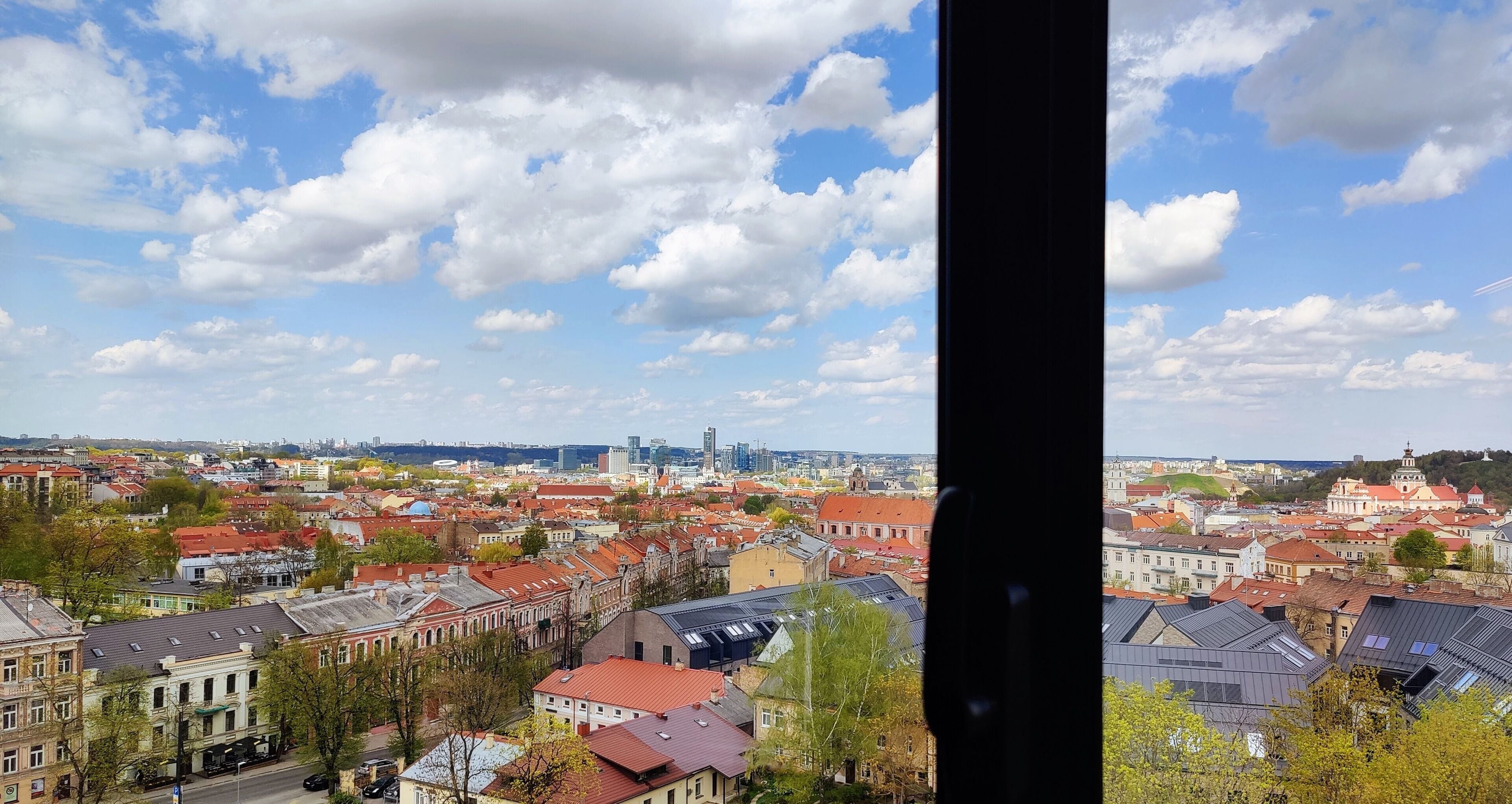 A panoramic view of a cityscape with a variety of building styles, including historical and modern architecture, and a clear sky with scattered clouds.