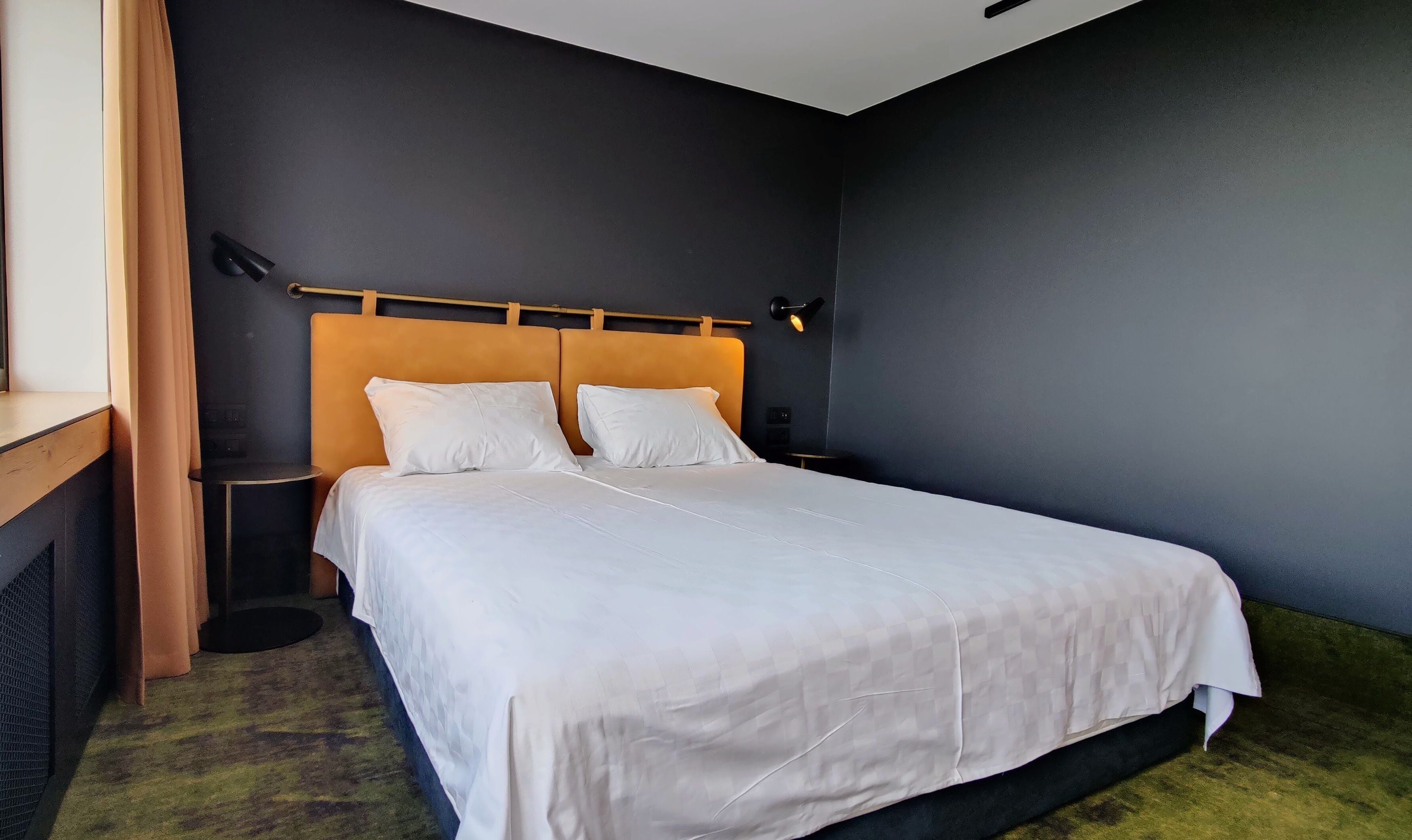 A neatly made bed with white linens in a room with dark walls and a wooden headboard.