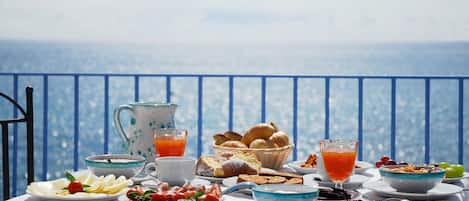 Mesa servida con alimentos para el desayuno, como pan, fruta y bebidas, con vistas a un paisaje pintoresco.