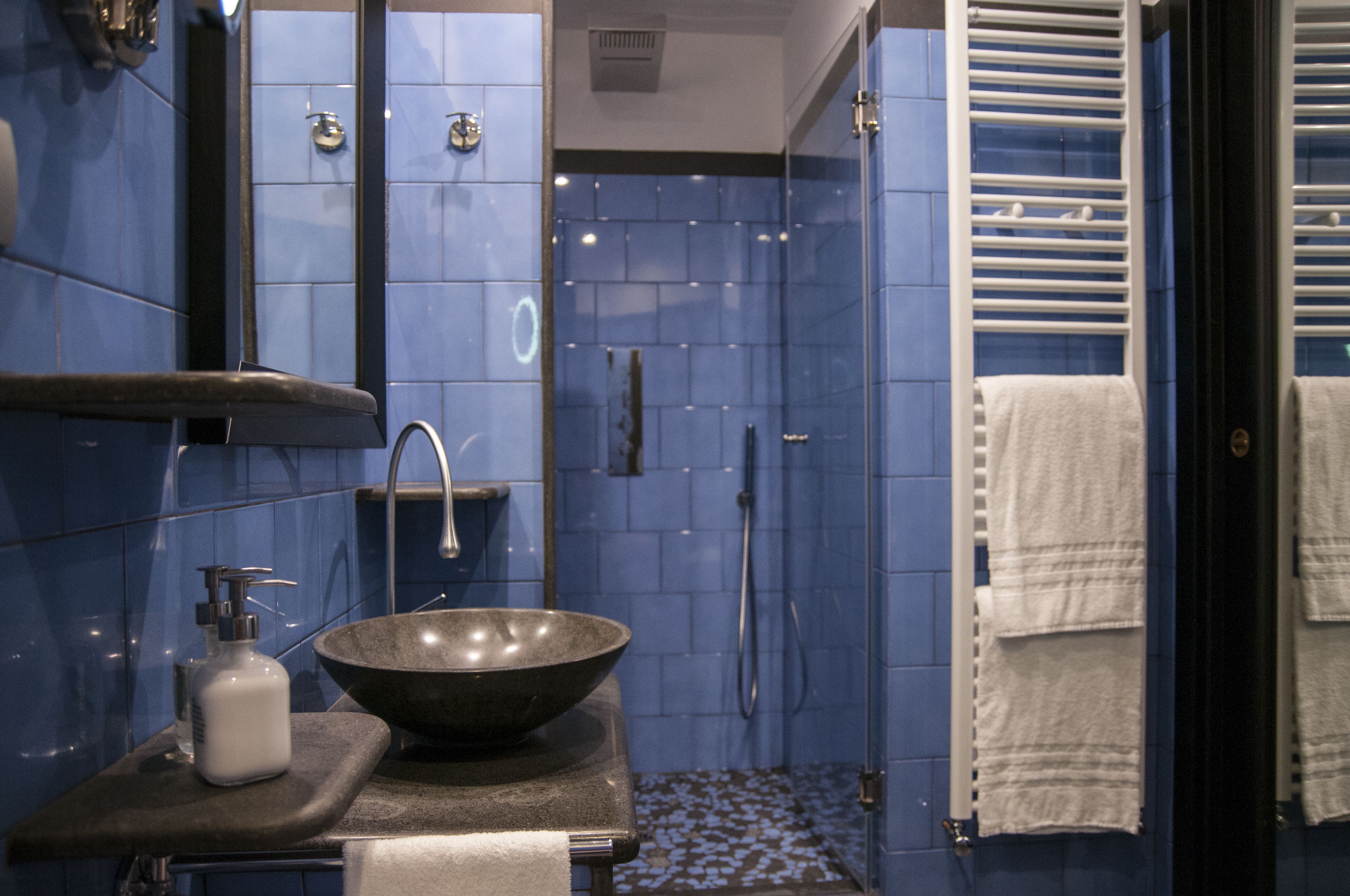 A bathroom with a large bowl sink, a mirror, and a shower with blue tiles.