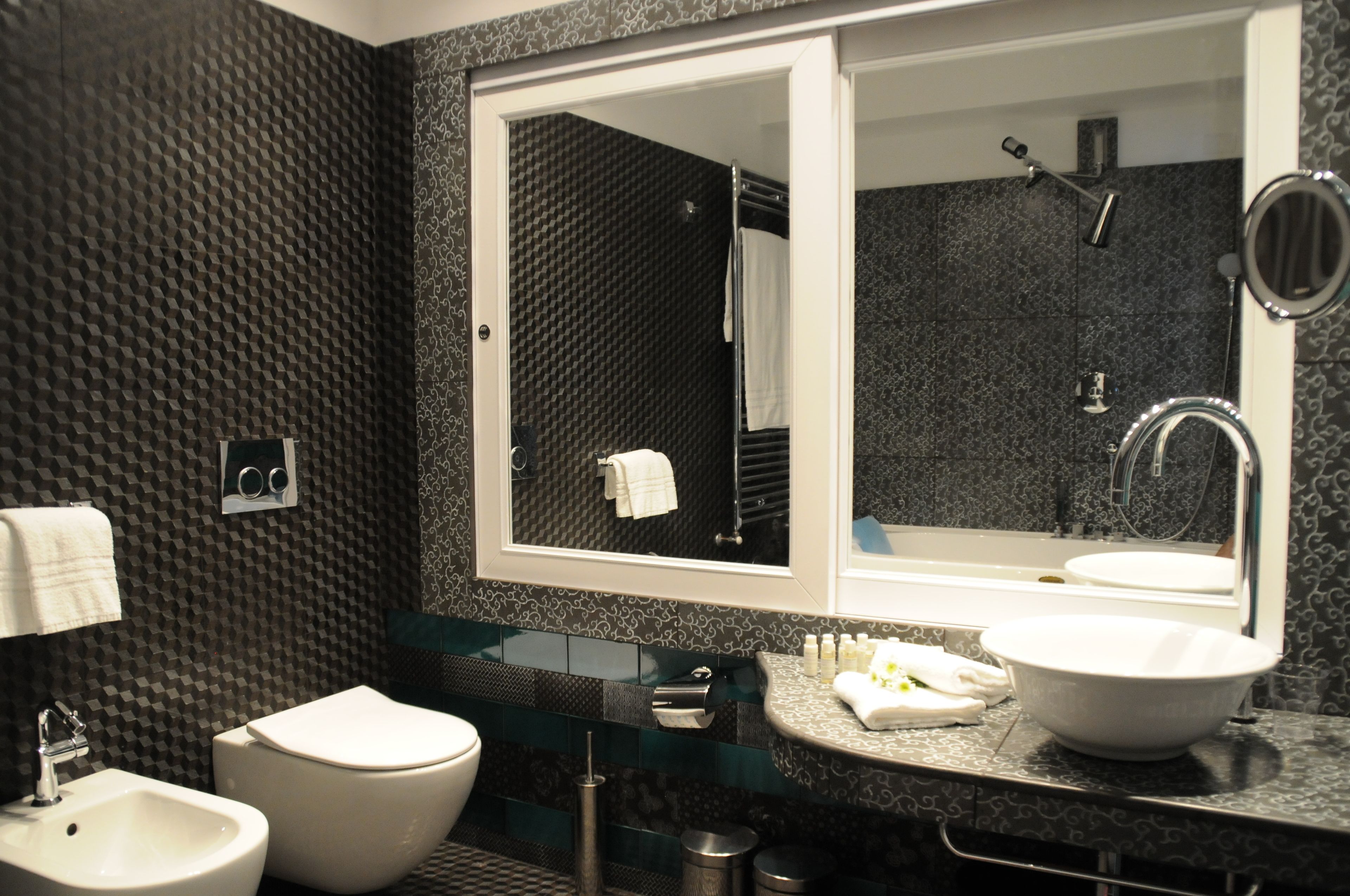 A modern bathroom with a large mirror, a toilet, a bidet, and a sink.