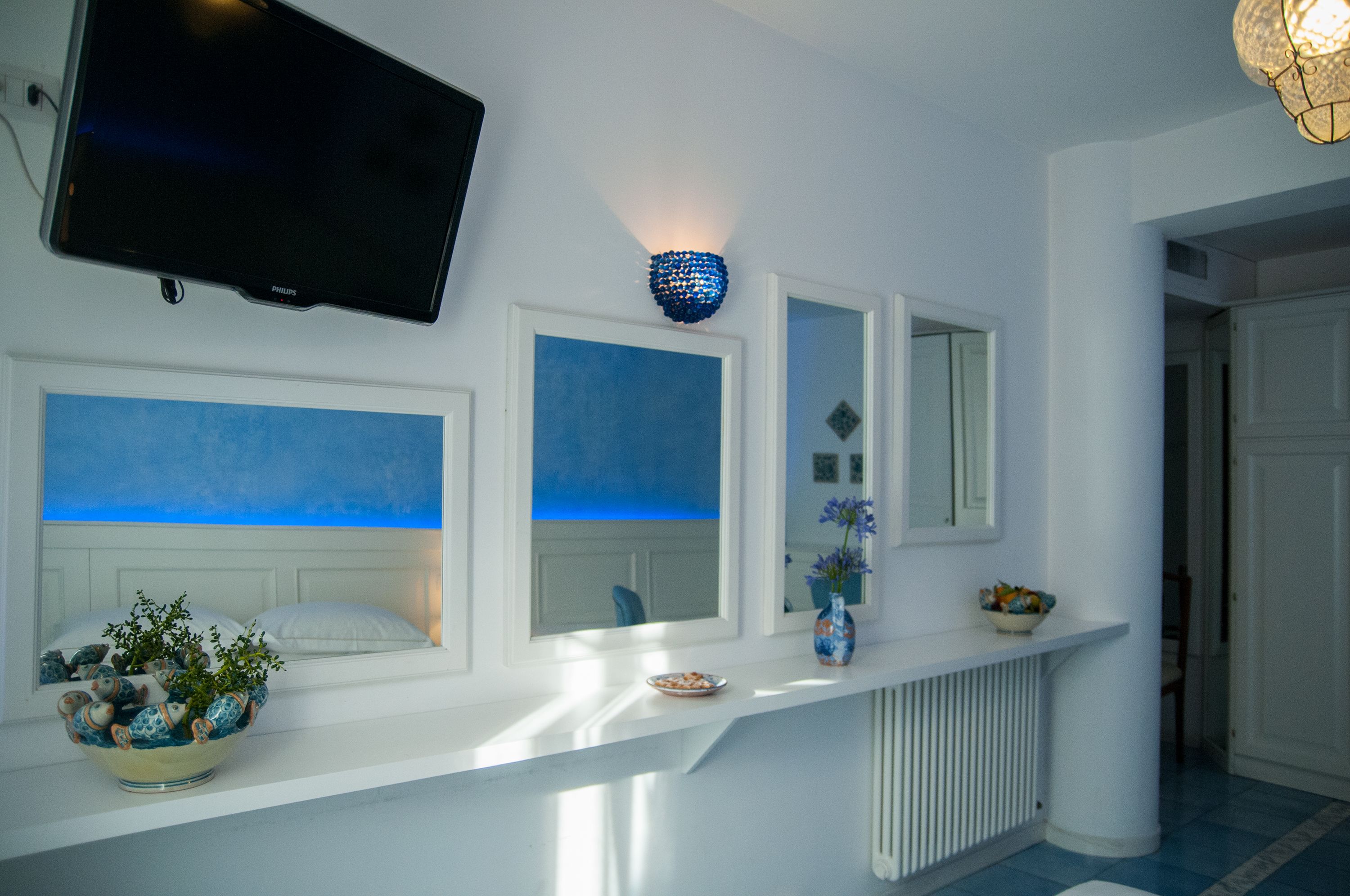 A modern bathroom with a white vanity, a mounted television, and a blue decorative light fixture.