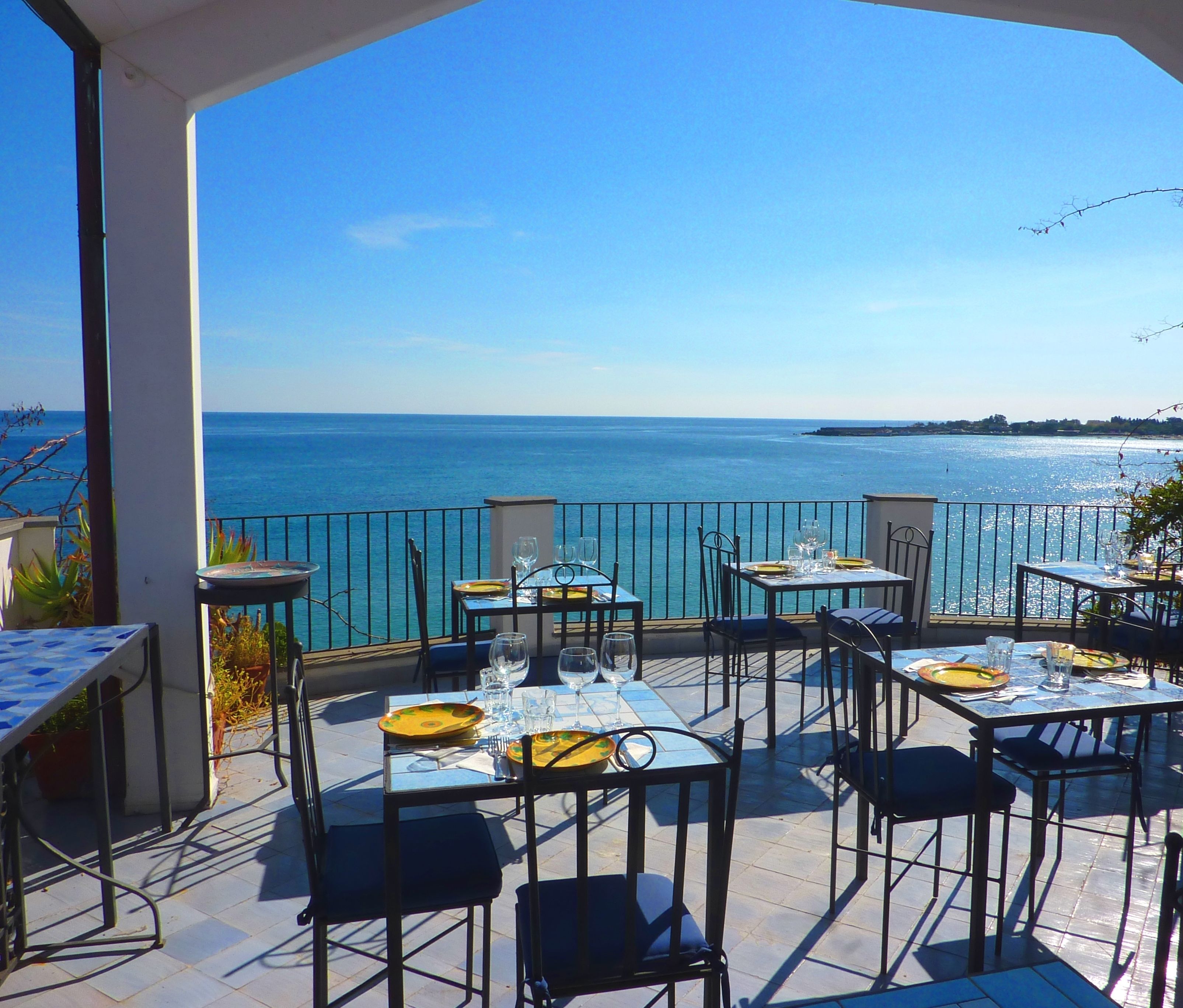 An outdoor terrace with tables and chairs, overlooking a body of water.