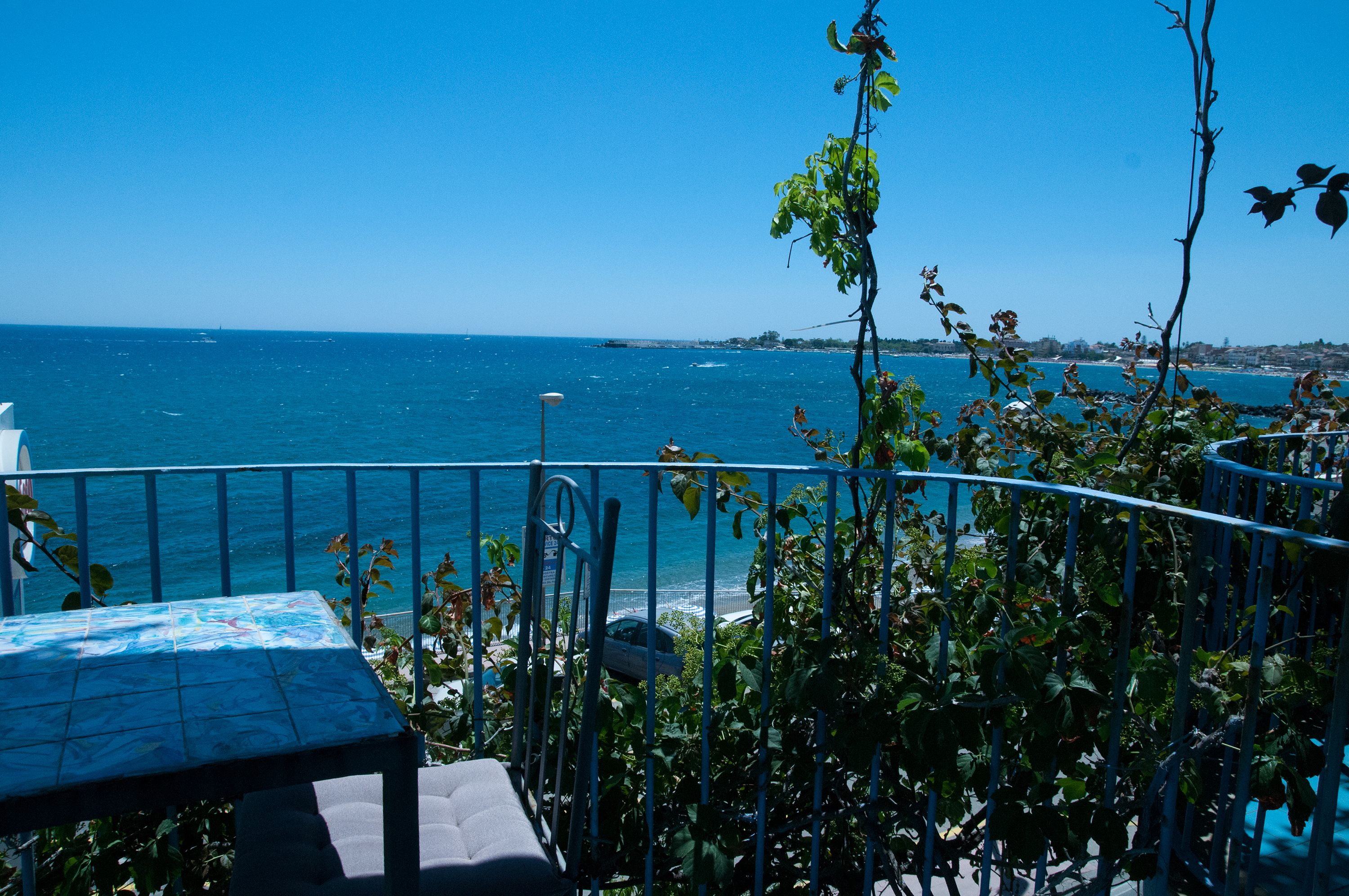 A balcony with a table and chairs overlooking the sea.