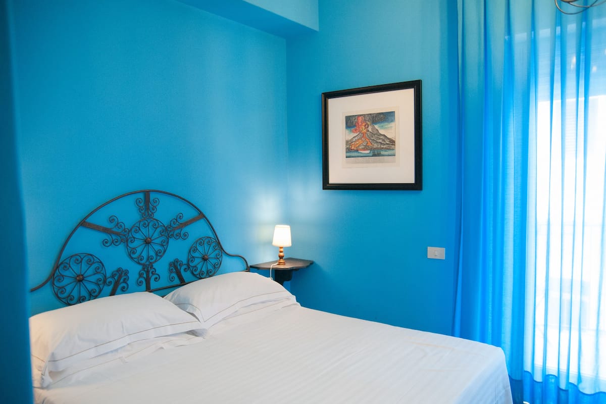 A bed with white linens, a metal headboard, a bedside table with a lamp, and a framed picture on the wall.