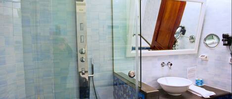 Une salle de bain dotée d’une douche à parois de verre, d’un lavabo avec un miroir au-dessus et d’un sol recouvert de carreaux de mosaïque bleus.