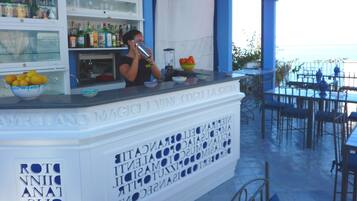 Un espace bar avec un barman, un saladier rempli de fruits et des étagères où sont rangées des bouteilles.