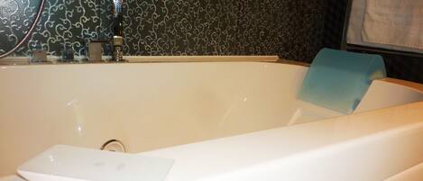 A bathtub with a "Jacuzzi" logo, a handheld showerhead, and a blue bath mat.