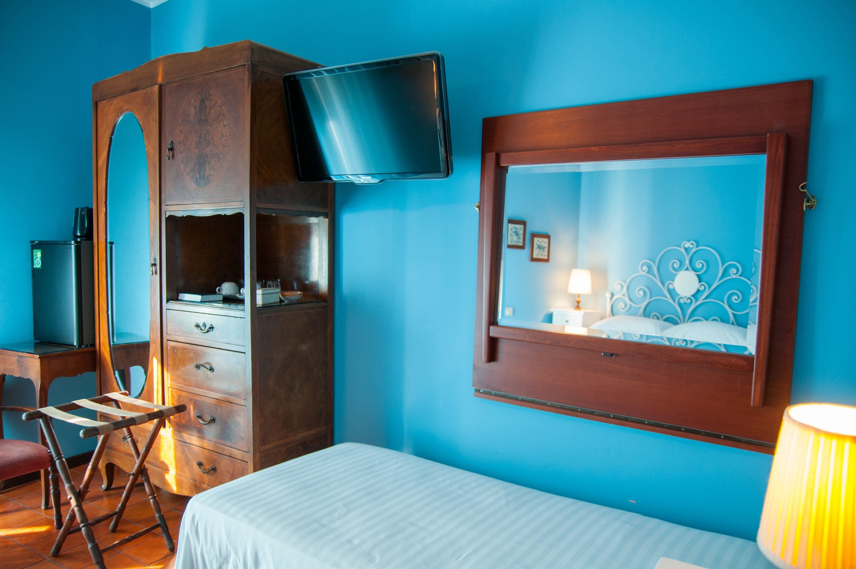 A room with a bed, a wooden wardrobe, a television mounted on the wall, and a window with a decorative frame.