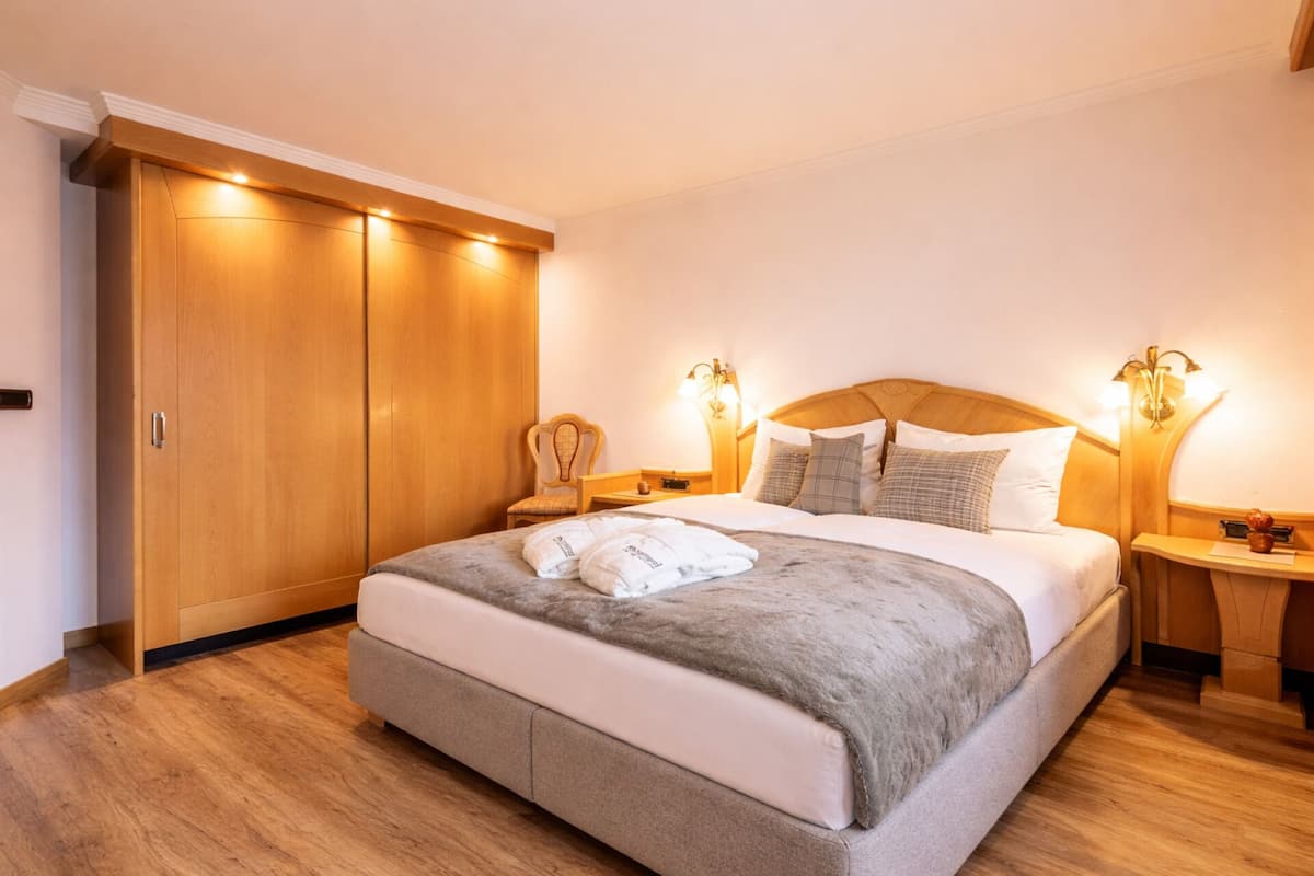 A hotel room with a large bed, wooden wardrobe, two bedside tables with lamps, and a chair.