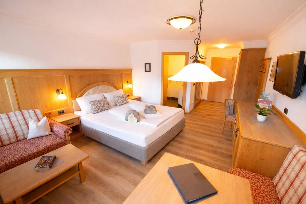 A hotel room with a bed, a sofa, a desk, and a television.