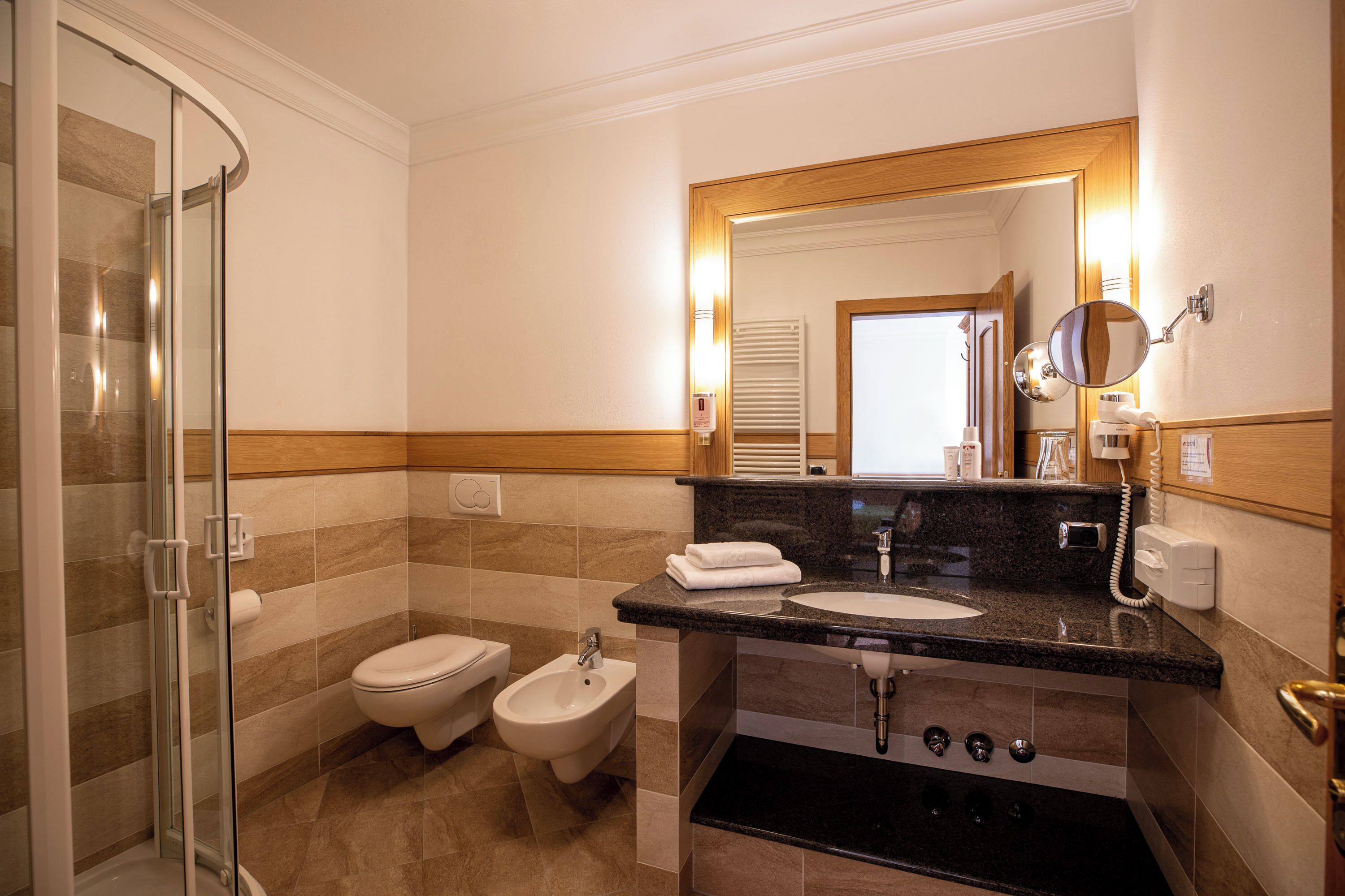 Ein Badezimmer mit Duschkabine aus Glas, einem Bidet, einem Waschbecken mit Waschtisch und einem Spiegel mit Beleuchtung.