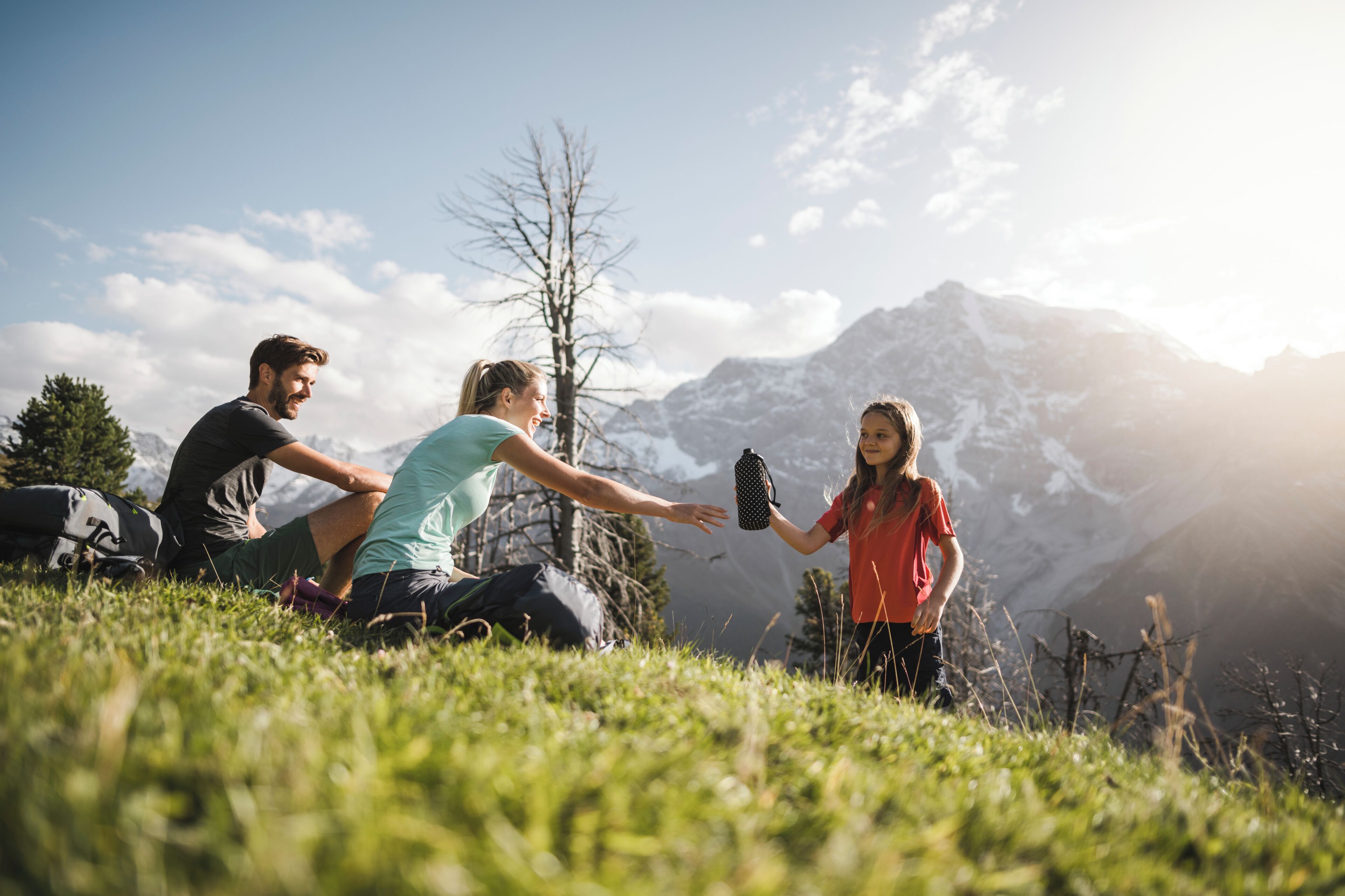 A group of people sitting on grass with mountains in the background.