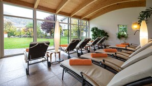 A spa area with reclining chairs, a wooden ceiling, and large windows offering a view of a garden and buildings. - Aktiv- & Wellnesshotel Zentral (Prato allo Stelvio)